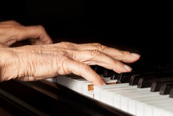Old person's hands playing the piano. Close up view of skin texture and piano keys.