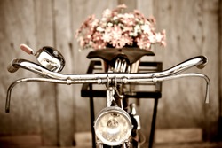 Old bicycle and flowers blur in background process in vintage old style film. Classic design bike with wood wall out focus behind.