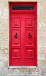 Bright red wooden door of a house with black doorknob rings