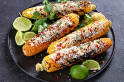Elote, Grilled Mexican Street Corn, charred cobs are slathered in sour cream based sauce, seasoned with chili powder and sprinkled with cheese, cilantro