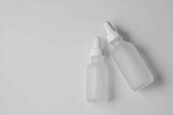 Two empty translucent glass dropper vials. Flatlay of different-sized bottles lying on white surface. Horizontal beauty and lifestyle background, mockup, and copy space. Professional lighting.