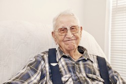 An elderly man sitting in a chair at his home, closeup with copy space