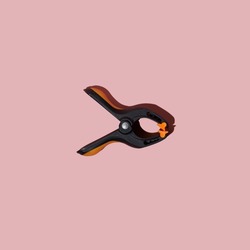 Plastic spring clamp isolated on pink background. Working hand tool. Black and orange spring clamp. Closeup.