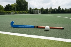Hockey stick and ball on grass field. Stick with customized text: Improve you performance