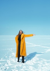 Young running woman in yellow coat walking on snowy ice. 