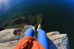 First person view of woman legs sitting on cliff edge with view of lake