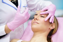 Aesthetic doctor injecting botulinum toxin into the forehead of her middle-aged patient.