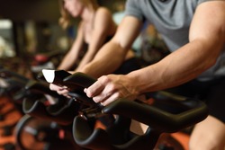 Close-up of hands of a man biking in the gym, exercising legs doing cardio workout cycling bikes. Couple in a spinning class wearing sportswear.