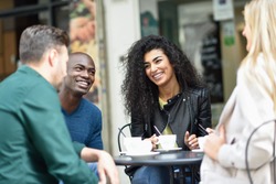 Multiracial group of four friends having a coffee together. Two women and and two men at cafe, talking, laughing and enjoying their time.