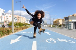Young fit black woman on roller skates riding outdoors on bike line. Smiling girl with afro hairstyle rollerblading on sunny day