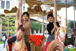 Cute little Asian siblings having fun on the horse of merry-go-round. 