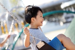 Cute Asian baby boy playing on a swing and having fun in park