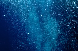 The picture shows underwater bubbles which raise from the depth of blue sea