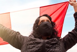 Peruvian woman with mask holds the Peruvian flag with her hands up