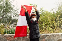 Peruvian woman wearing a chullo and mask raising the flag of Peru