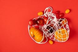 Multicolored yellow, black, red tomatoes in a white mesh shopping bag on a red background, top view