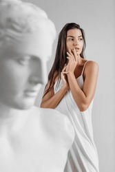 Portrait of young beautiful woman standing near gypsum sculpture Venus face