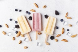 Homemade frozen ice cream popsicles from fruits and berries on table whith flowers and ingridients, top view