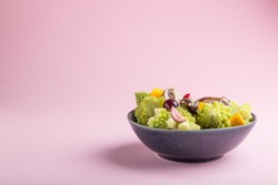 Vegetarian salad from romanesco cabbage, champignons, cranberry, avocado and pumpkin on a pastel pink background. side view, copy space.