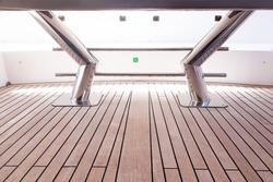 Teak deck of a yacht and stainless steel stanchions with teak deck reflection on them, close-up.