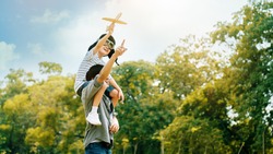 Lifestyle Asian family Father and son sat on his shoulders and run in  park. Paper plane as a toy in hand of kid And there are many big trees in garden Is natural in the morning of summer