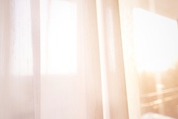 Very bright, soft shot of transparent, white curtain blocking some sun light and heat from outside of residence building during sunrise time with radiation of sunlight over area. For use as background