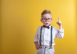 Portrait of stylish little boy with finger pointed up. Little child in glasses has idea. Kid isolated on yellow blackboard. Success, bright idea, creative ideas and innovation technology concept.