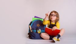 Children go back to school. Little happy  girl doing homework at home with backpack full of books, pencils. Pupil reading a book, writing and painting.  Kid is drawing. Child in glasses. 