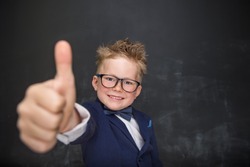 Child boy with thumb up on chalkboard dreams to be a businessman. Nerd school boy in glasses showing ok sign. Strong, confidence, success, possible, innovation. Go back elementary school