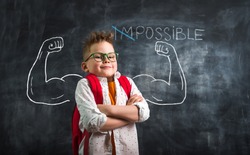 Change impossible on possible. Funny kid with strong arms against blackboard