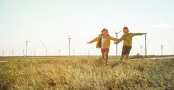 Little girl and boy are running in front of windmills. Renewable energies and sustainable resources - wind mills. children playing with the wind near a wind turbine
