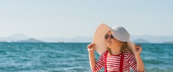 Baby girl in hat and sun glasses on the summer beach. Kid in striped t-shirt on the sea.