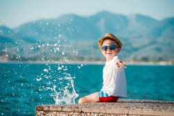Little happy boy in blue sunglasses and hat has a big smile on his face. Beautiful landscape and bright beach. Blue summer sky and sea water background. Kid on summer vacation. text. copy space
