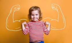 Funny strong child with muscles over yellow wall. Nerd kindergarten kid girl showing bicep muscles. Dream, confidence, success, possible, innovation. Go back elementary school.