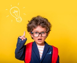 Child boy in eyeglasses isolated on yellow paper wall. Excellent idea, kid with illustrated bulb. Happy smiling kid go back to school, kindergarten. Success, motivation, winner, genius concept.