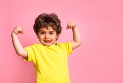 Portrait of little kid boy isolated over pink background showing tongue. Funny little power super hero kid showing muscles. Strength, confidence or defense from bullying. Kindergarten or school kid