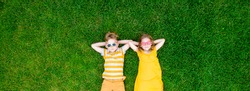 Kids boy and girl lying on the green grass. Happy children in cool yellow clothes from above. Top view. Child in sunglasses. Blond kids with freckles looking in camera