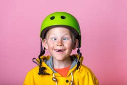 funny kid boy portrait. crazy comic blond child makes grimace and crosses eyes. school boy with broken front tooth playing fool in green protect helmet and yellow coat. bright people face expressions.