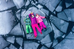 Top view of people lying on ice alone. Woman and children in bright clothes on broken ice block in water. Winter cracked ice on lake with kids. Danger fun. Playing sustainable. Climate global warming.