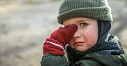 Little migrant child cry. Portrait of kid boy wipes tears. Evacuation children. War Ukraine