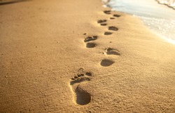 Footprints at sunset with golden sand. beach, wave and footsteps at sunset time