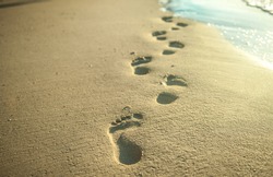 bare footsteps on the sand on a beach. the sand is white and the steps can be of man or women. Footsteps on the coral sandy beach