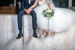 Beautiful wedding couple sitting on wooden pier, swung their legs and enjoying wedding.