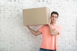 Handsome man carrying heavy box in front of white brick wall background