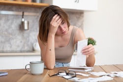Close up of shocked woman sitting at the table, stressed and confused by calculate expense from invoice or bills, have no money to pay mortgage or loan. High prices and spending money concept