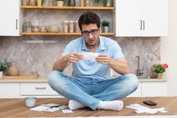 Stressed man sitting on the table and holding many bills in his hands in a spending, taxes and debt concept	