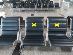 Chairs or benches for visitors in lounge or hall for passengers in airport or railway station with warning marks on prohibited seats regarding covid-19 pandemic security measures of social distancing.