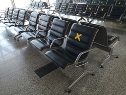 Chairs or benches for visitors in empty lounge for passengers in airport or railway station with warning marks on prohibited seats regarding covid-19 pandemic security measures of social distancing.