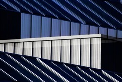 Architectural surfaces. Corrugated  metal structure and framed glass wall of industrial building. Modern architecture photo. Hi-tech material background. Polygonal geometric pattern of parallel lines.