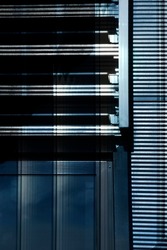 Window with blinds. Industrial or office building. Close-up of modern architecture. Hi-tech material structure of wall with glass and metal texture. Geometric pattern of rectangles and parallel lines.